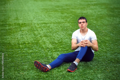 Young smiling sportsman sitting on grass