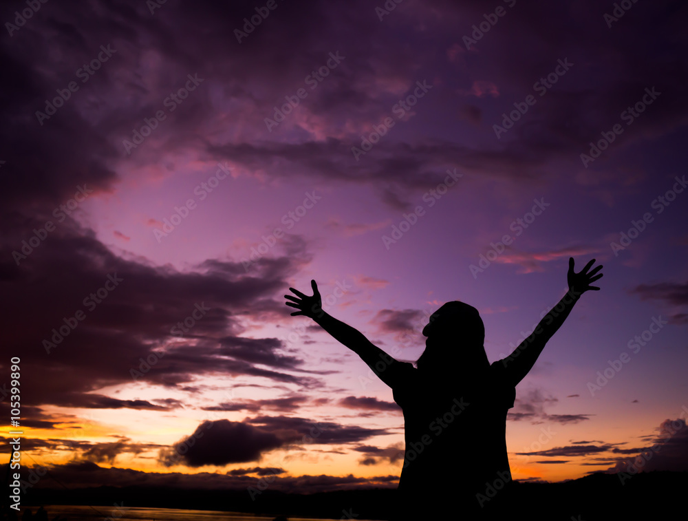 Silhouette of young woman standing against sunset with beautiful