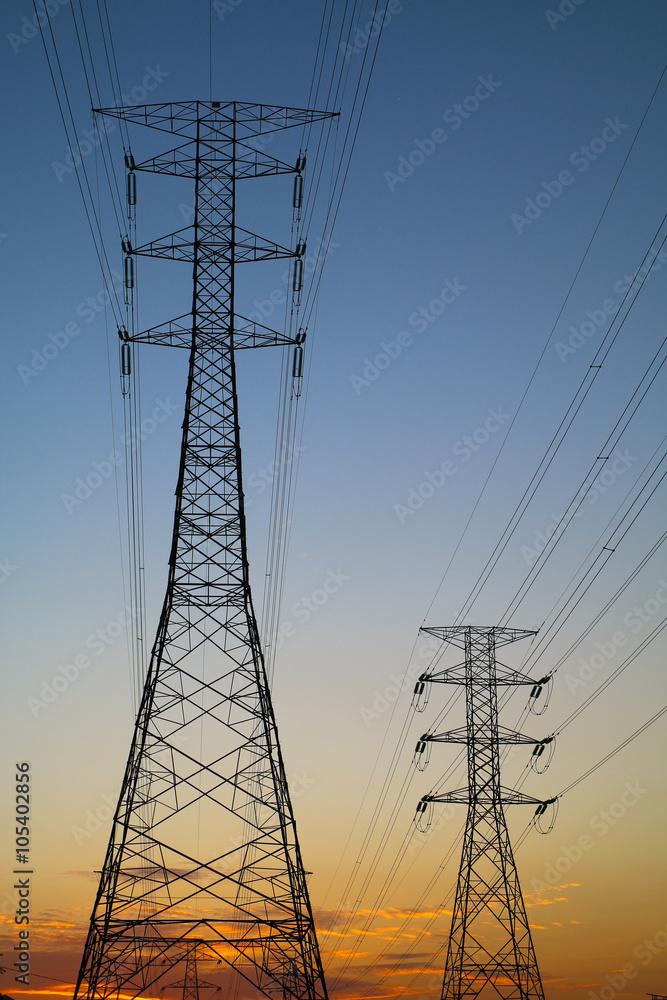 Silhouette of grid energy towers against sunset sky
