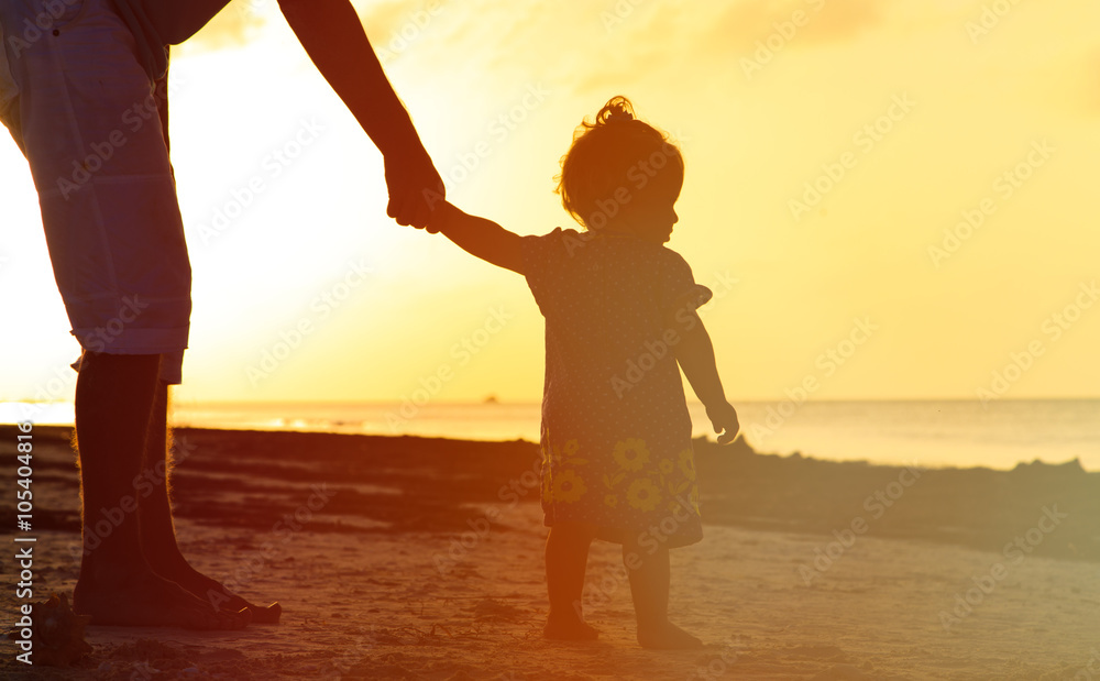 Fototapeta premium Silhouette of father and little daughter walking at sunset