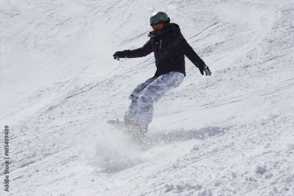 Young snowboarder woman sliding downhill and brake sharply.