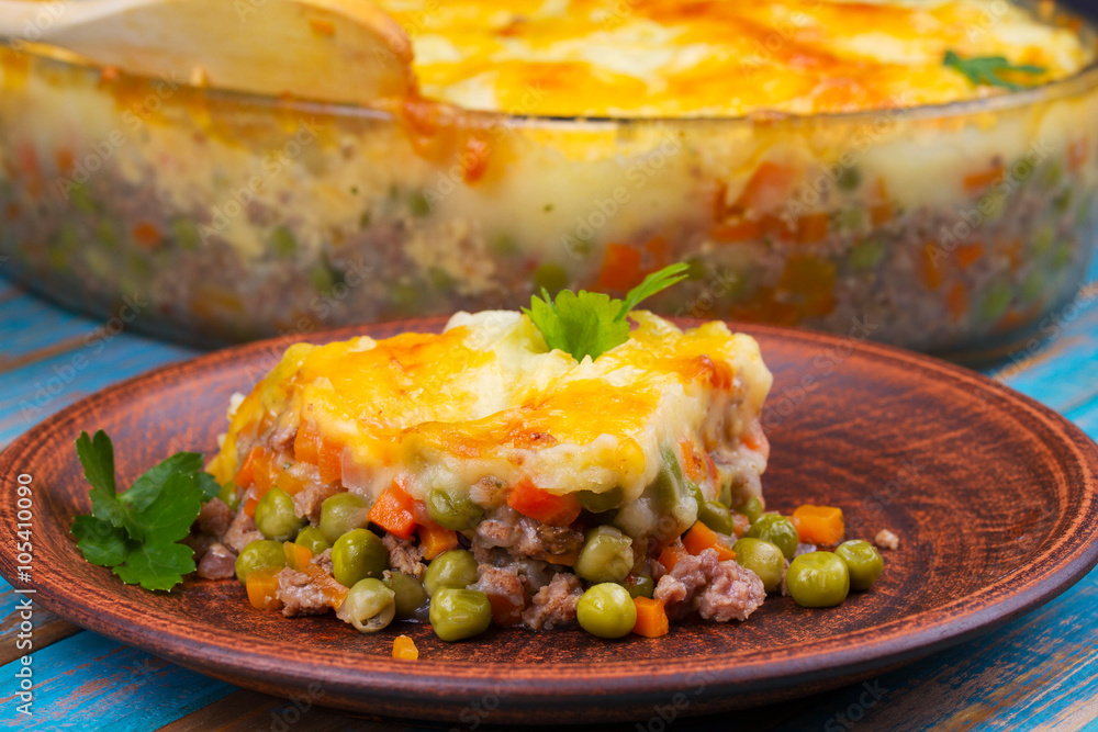 Potato, cheese, meat, carrot, onion and green peas casserole on blue wooden background Potato, cheese, meat, carrot, onion and green peas casserole on blue wooden background