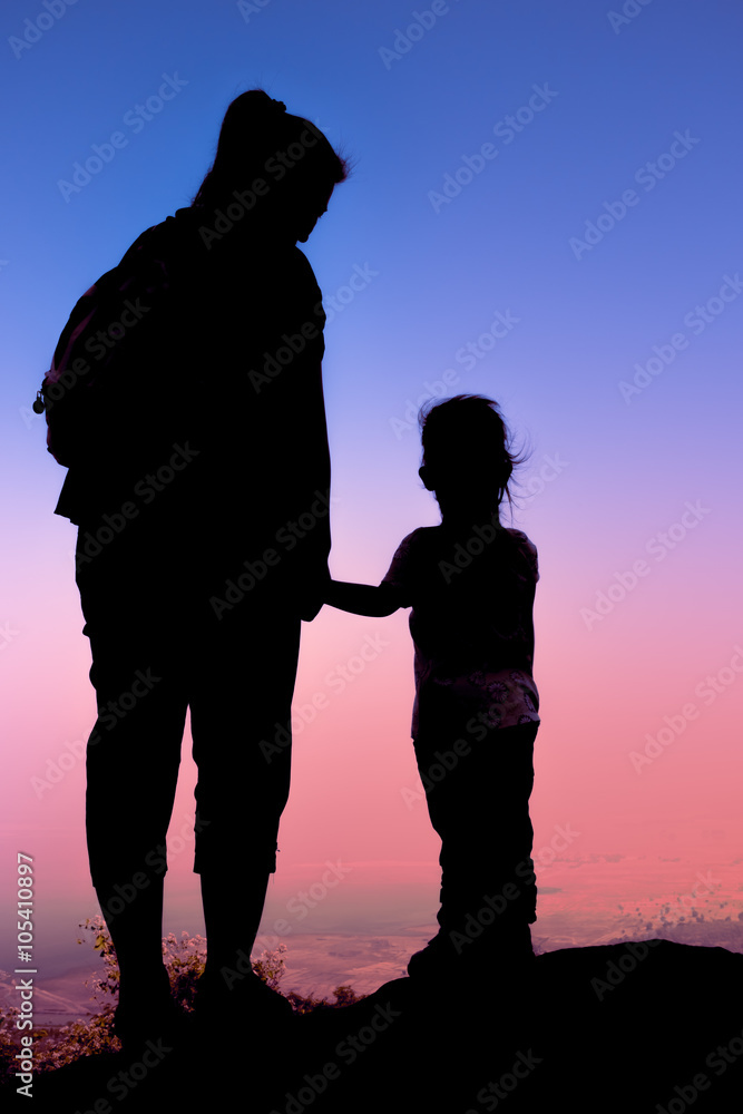 Silhouette of mother and child hikers enjoying the view at the top of a mountain. 