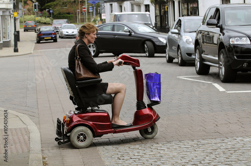 Woman seated on a mobility scooter crosses the road at a pedestrian crossing