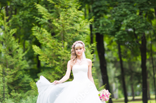 Beautiful bride with wedding bouquet of flowers outdoors in green park.