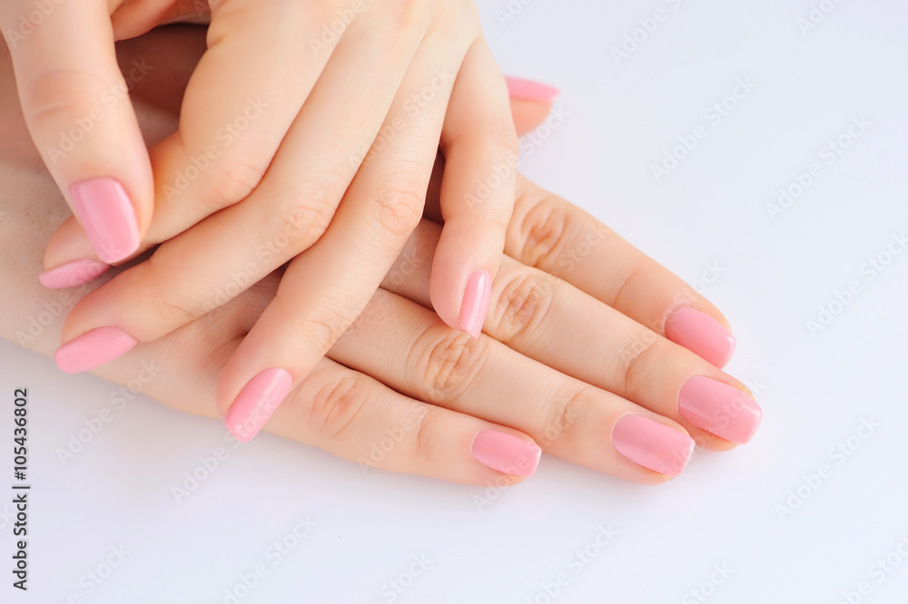 Closeup of hands of a young woman with pink manicure on nails against white background