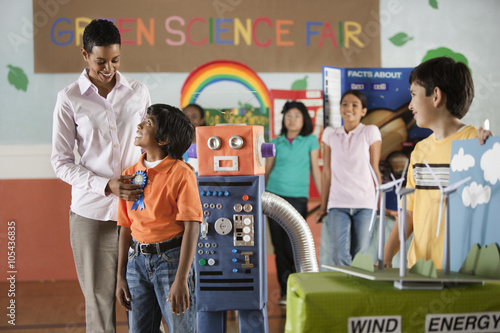 A group of students and a teacher awarding a prize to a boy standing beside a robot model,  photo