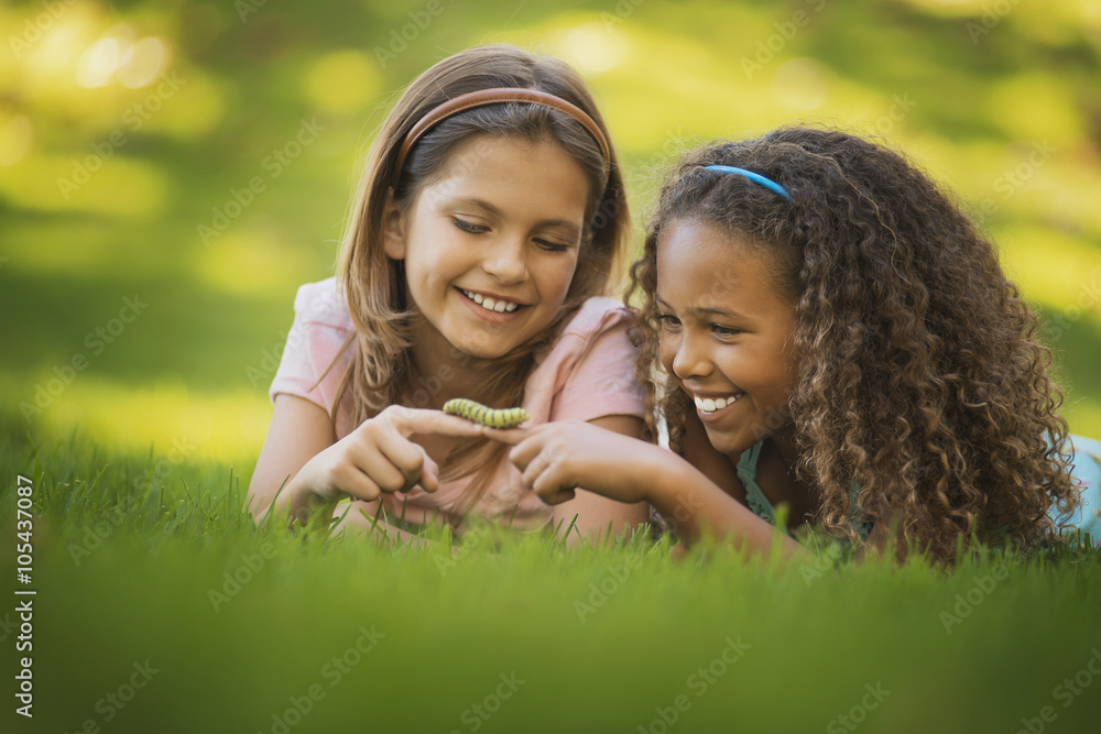 Two girls lying on the grass, one holding a green caterpillar on her finger, Two girls lying on the grass, one holding a green caterpillar on her finger,