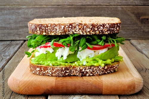 Superfood sandwich with avocado, egg whites, radish and pea shoots on whole grain bread against a rustic wood background