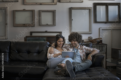 Loft decor, A wall hung with pictures in frames, reversed to show the backs, A couple on a sofa, looking at a digital tablet, photo