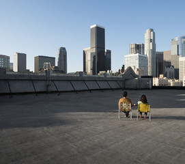 A couple, man and woman sitting in deck chairs on a rooftop overlooking city skyscrapers, 