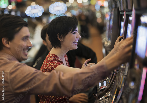 Two people, a young man and woman, playing the slot machines in a casino, 