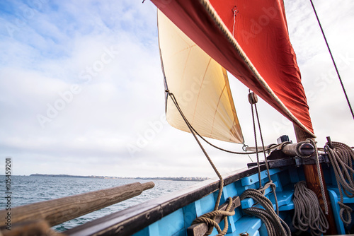 Fototapeta beige cotton jib sail and an ocher sail filled by the wind with wooden mast, bow