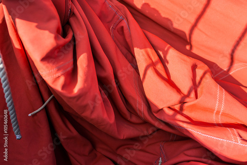 cotton ocher sail of a vintage sailing boat with ropes, wrinkle, seam and a blur background