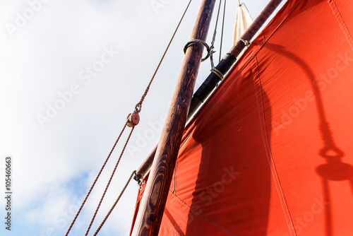 ocher sails of a vintage sailing boat blew up by the wind with his wooden mast, yardarm and ropes during a sunny sea trip with the blue sky behind  photo