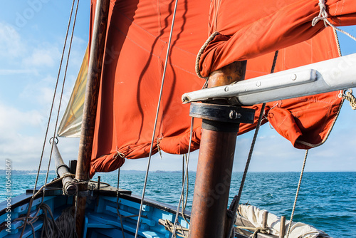 bow of an old wooden blue sailing boat with a cotton vintage ocher sails, wooden mast, white jib and ropes during a sunny sea trip