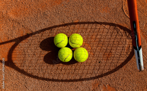 Cztery piłki tenisowe w cieniu rakiety do tenisa ziemnego.