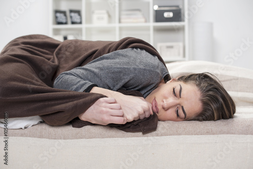 Girl who does not feel good lying on the bed covered with a blanket