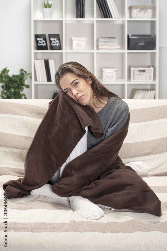 Girl wrapped in a brown blanket sitting in the living room on the bed Girl wrapped in a brown blanket sitting in the living room on the bed