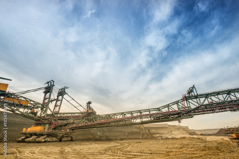 One side of huge coal mining drill machine photographed from a ground with wide angle lens. Dramatic and colorful sky in background. One side of huge coal mining drill machine photographed from a ground with wide angle lens. Dramatic and colorful sky in background.