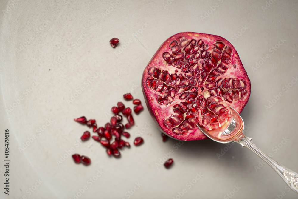 Fototapeta premium Half a Pomegranate with a spoon sticking out, shot on a grey bac
