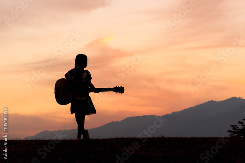 a silhouette of a girls standing with her guitar.