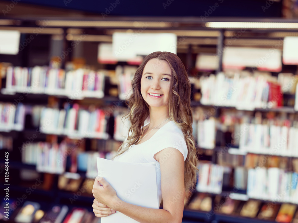 Happy female student holding books at the library Happy female student holding books at the library