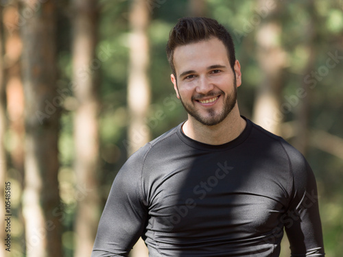 Smiling handsome muscular young man standing outdoors in a woode