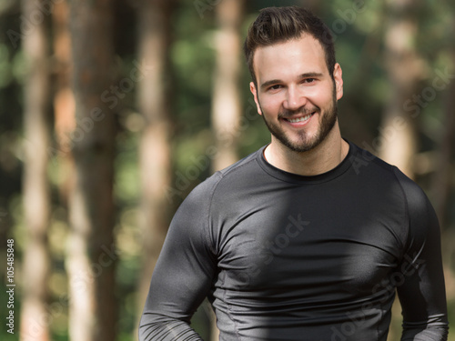 Smiling handsome muscular young man standing outdoors in a woode