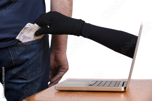 Internet theft - a gloved hand reaching through a laptop screen to steal cash from a person s pocket.
