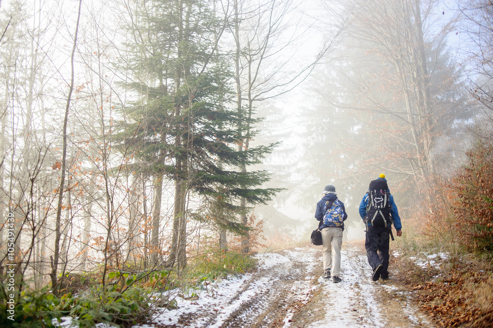 Man and woman backpackers hiking on foggy forest mountain trail in winter/late autumn. Rear view. Man and woman backpackers hiking on foggy forest mountain trail in winter/late autumn. Rear view.