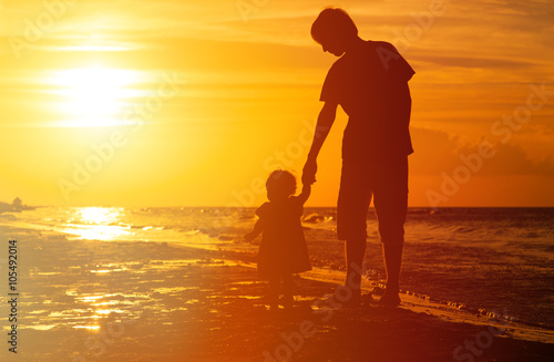 silhouettes of father and little daughter walking at sunset