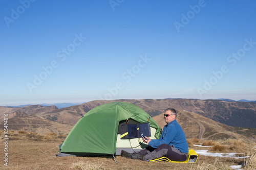 The solar panel attached to the tent. The man sitting next to mobile phone charges from the sun.