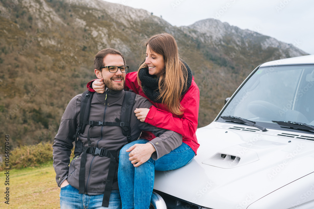 Smiling young couple in love leaning on car, hiking outdoor on vacation, enjoying relaxing rural holidays.