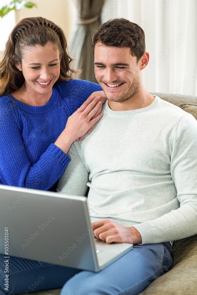 Young couple smiling face to face on sofa and using laptop Young couple smiling face to face on sofa and using laptop