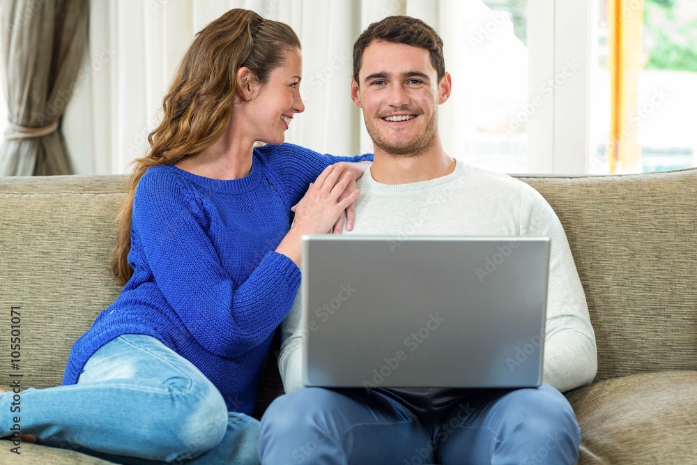 Young couple smiling face to face on sofa and using laptop Young couple smiling face to face on sofa and using laptop