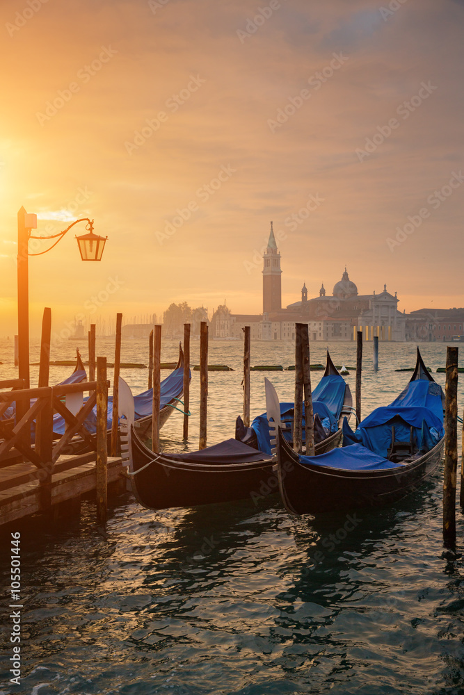 Fototapeta premium Gondolas by Saint Mark square during sunrise with San Giorgio di Maggiore church in the background in Venice Italy