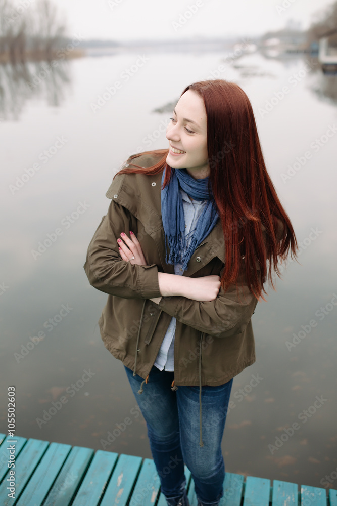 Woman standing on pier at the river in a cold cloudy day and smile