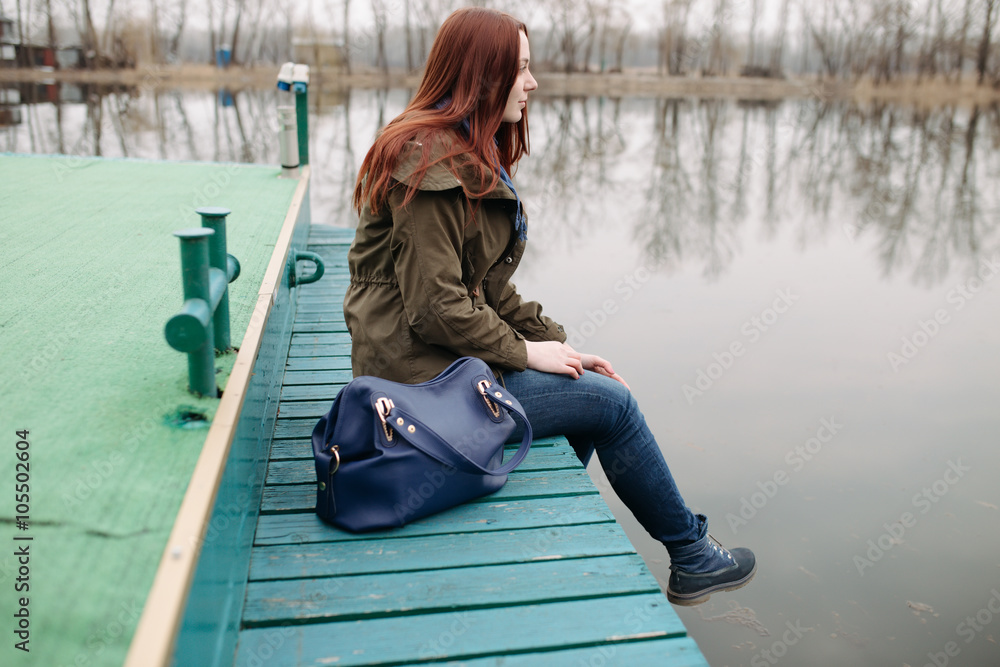 Young woman sitting on pier at the river in a cold cloudy day Young woman sitting on pier at the river in a cold cloudy day