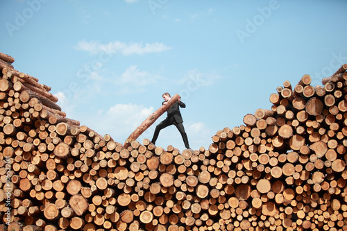 Foto business vision - hardworking businessman on top of large pile of cut wooden log