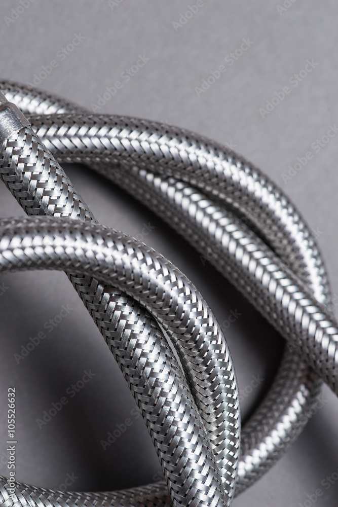 Obraz premium Braided stainless steel water hose over grey background