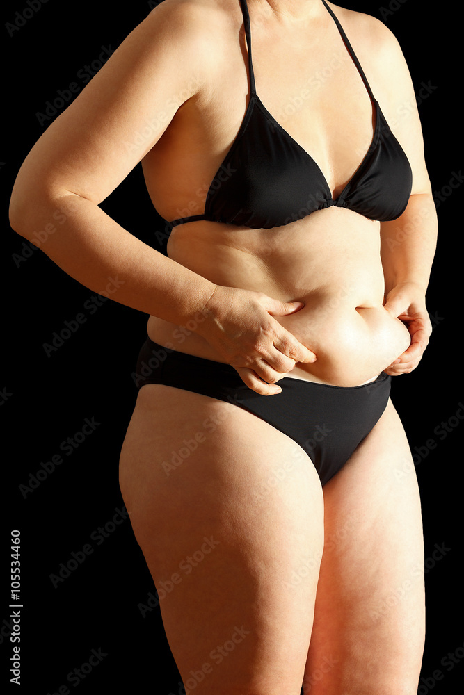 Naklejka premium Woman in bikini with flabby stomach holding the excessive fat or fupa in her hands, black background