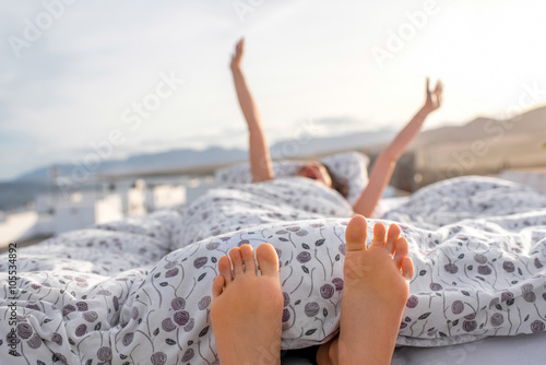 Young and cute woman waking up lying on the bed on the roof top with white houses on the background. Good morning concept