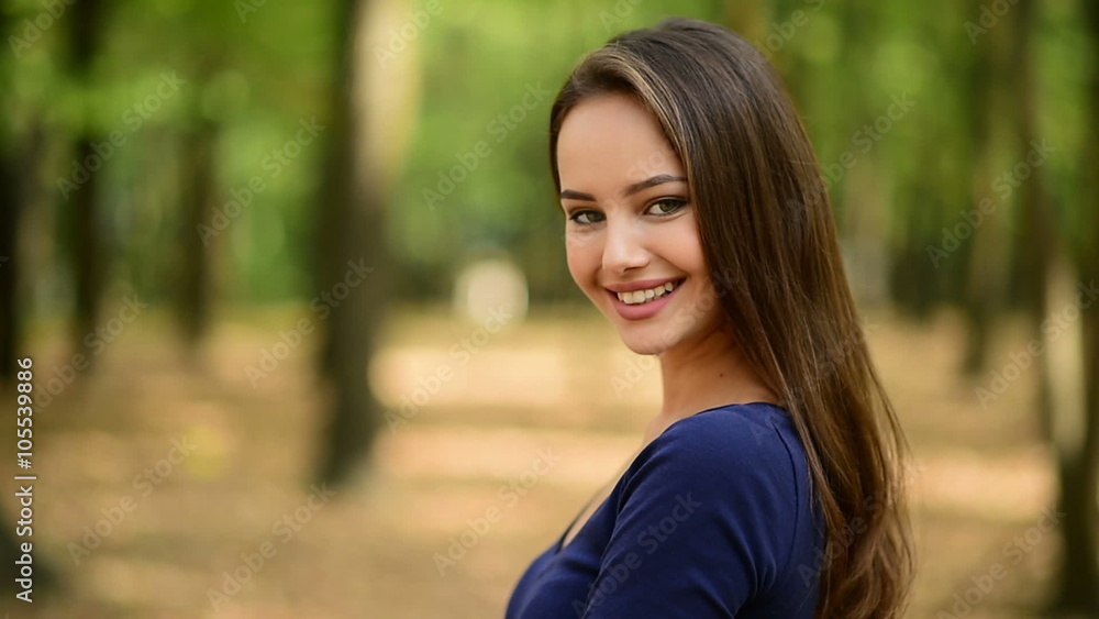 Beautiful smiling young woman with long hair turns around and looking at camera of the summer park. Outdoor Beautiful smiling young woman with long hair turns around and looking at camera of the summer park. Outdoor