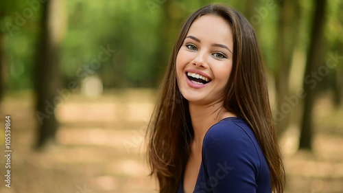 Beautiful smiling young woman with long hair  turns around and looking at camera of the summer park. Outdoor. Slow motion
