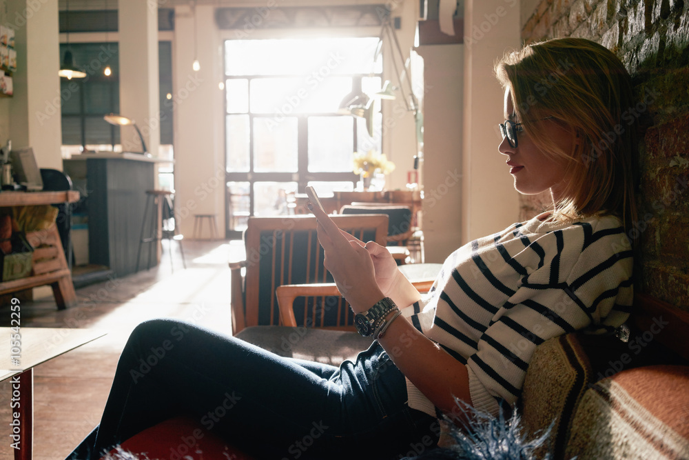 Beautiful blonde girl working at a coffee shop with a smart-phone. female freelancer connecting to internet via cellphone. flare light Beautiful blonde girl working at a coffee shop with a smart-phone. female freelancer connecting to internet via cellphone. flare light