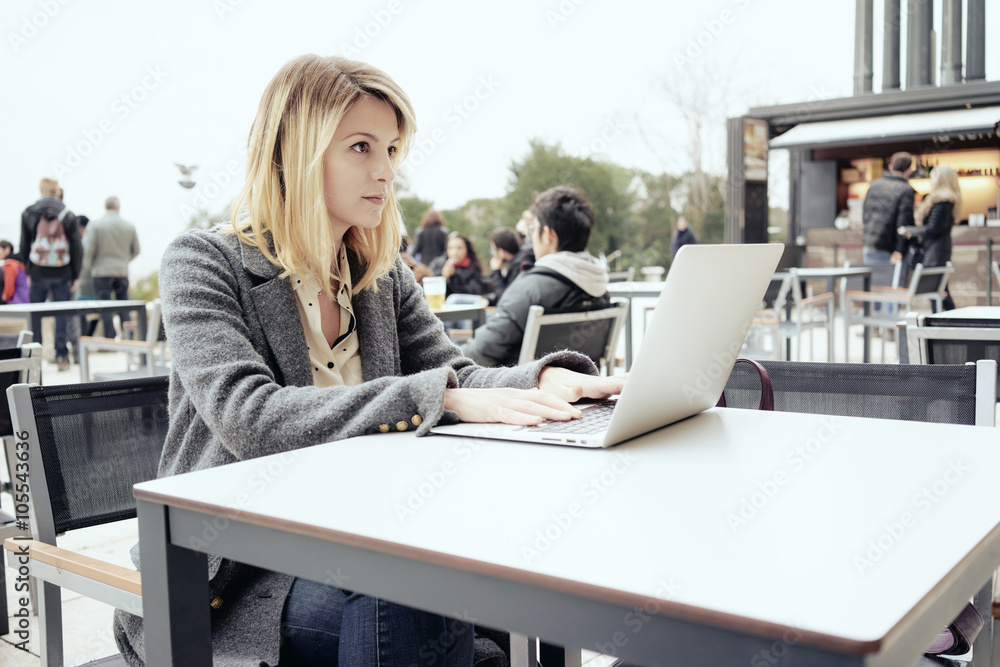 young beautiful female freelancer with blonde hair working in a coffee-shop outside with  laptop computer