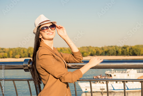 Stylish young woman in glasses standing on the embankment and sm