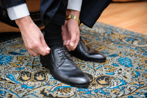 groom ties the laces on black wedding shoes