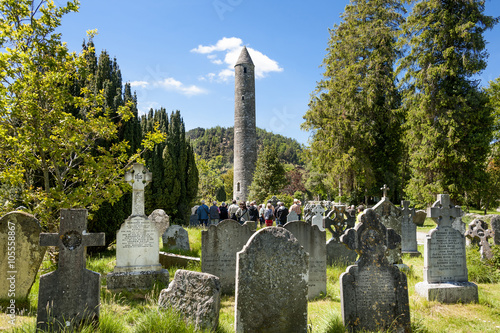Roundtower with graveyards and tombstones in the foreground Glendalough Ireland photo